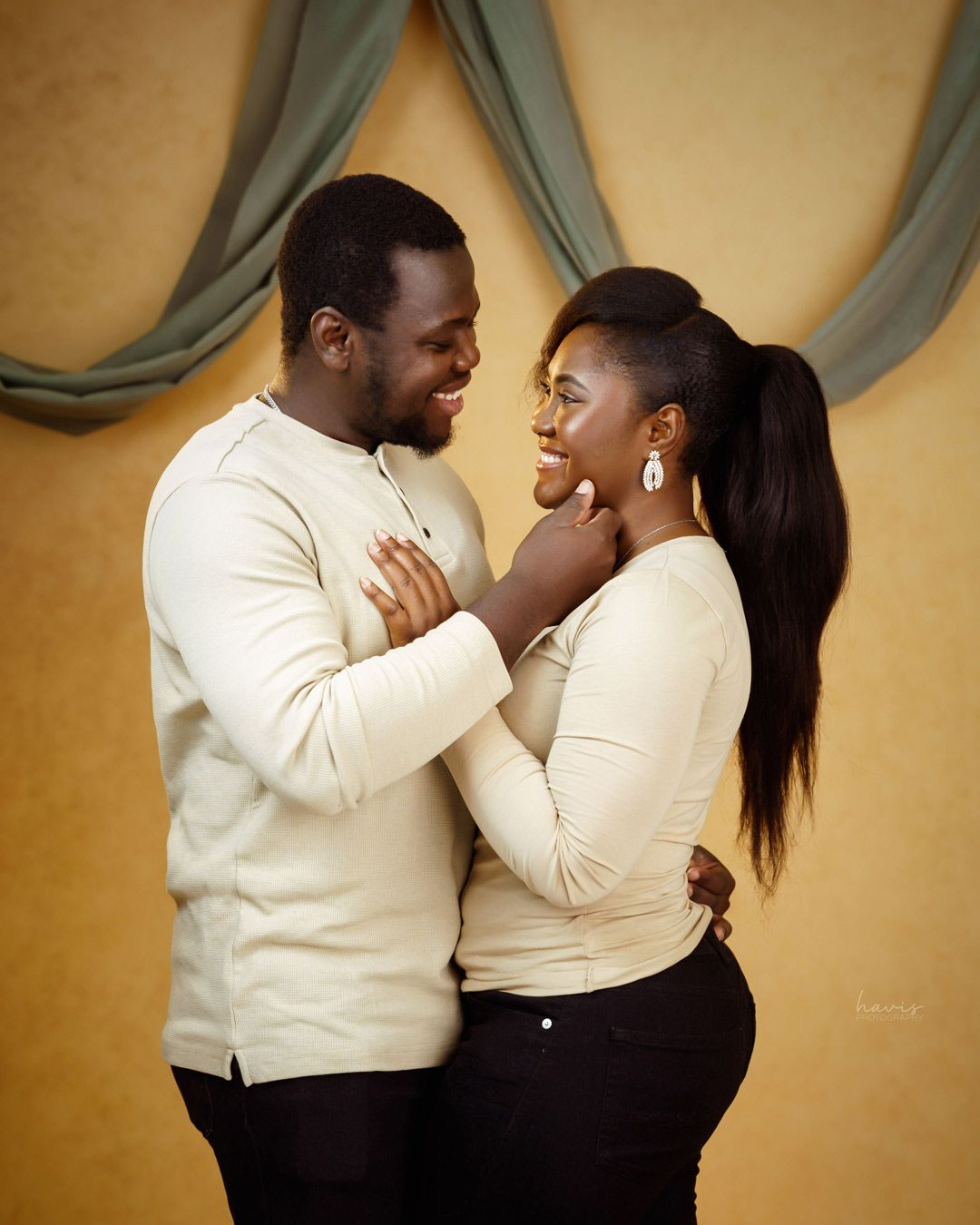A couple looking into each other's eyes and smiling for a photograph in front of a beige background