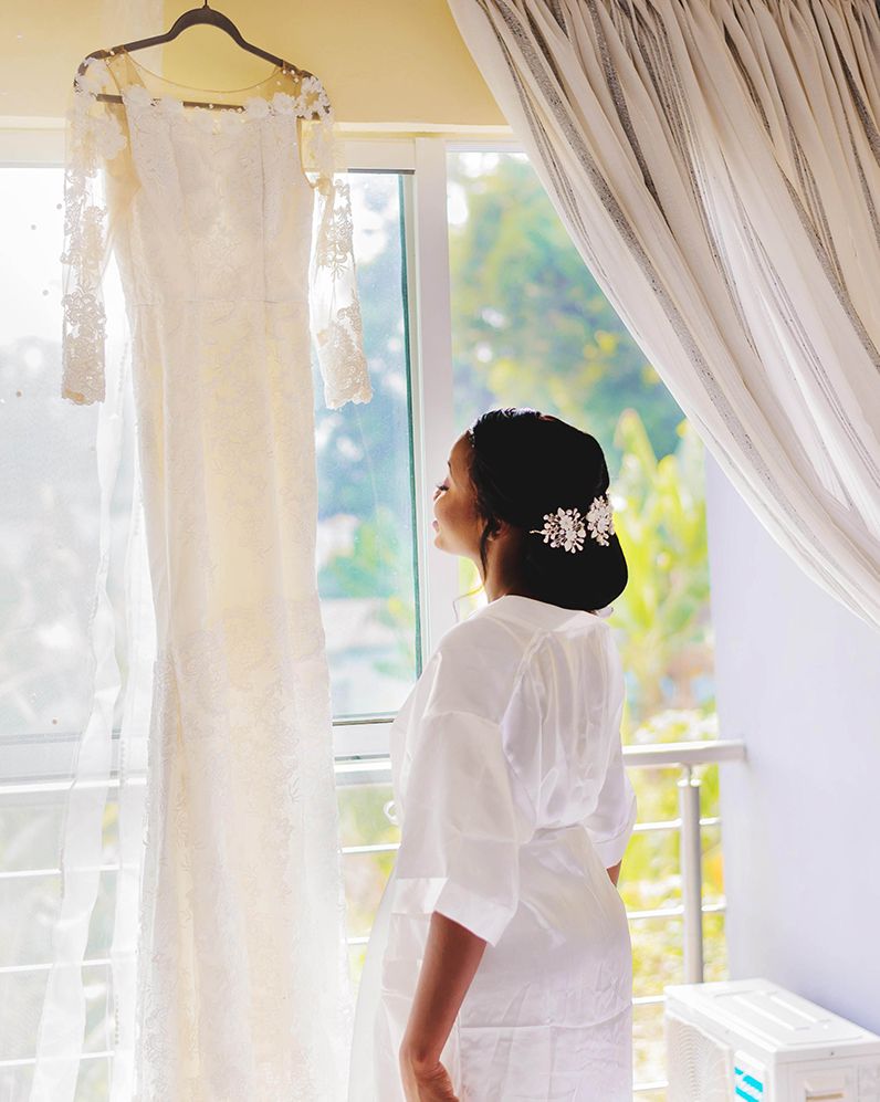 A bride in her bridal robe looking and smiling at her wedding gown on an hanger