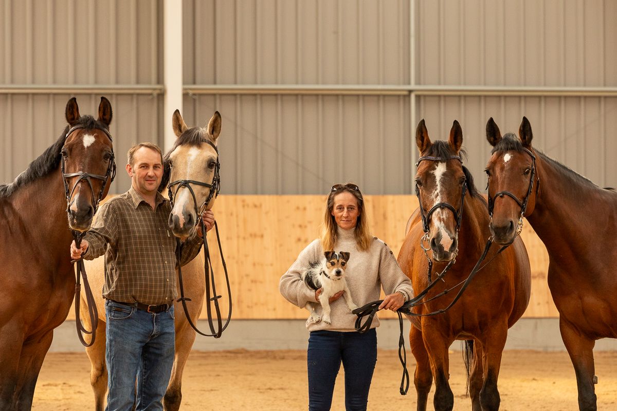 Four beautiful horses and their handlers stand together in an indoor riding arena.