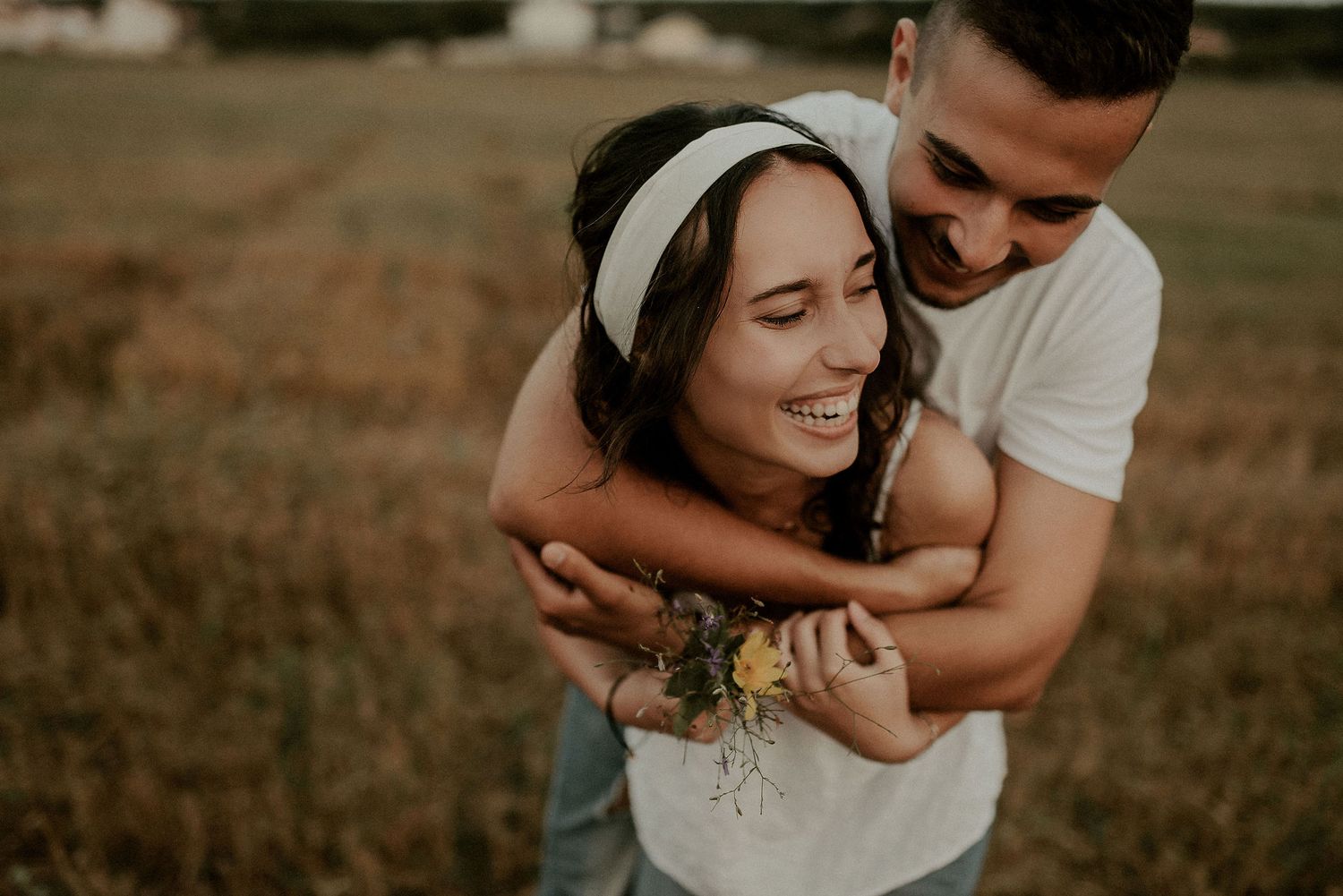 Couple embracing in golden field during sunset photoshoot.