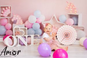 First birthday setup with balloons, decor and 'ONE' lettering in soft pink tones.