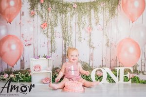 Baby's first birthday scene with pink balloons and 'ONE' lettering against floral backdrop.