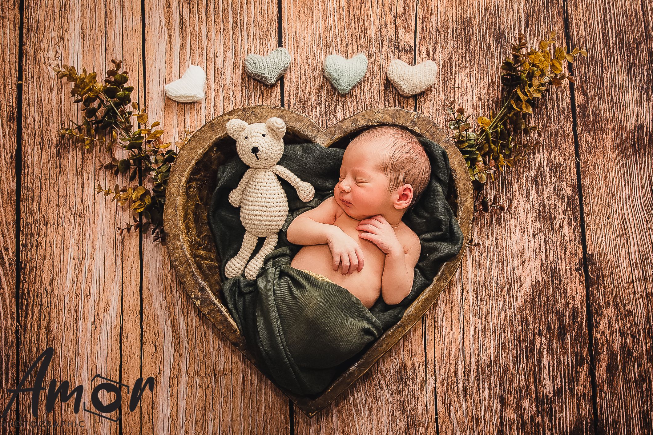 Heart-shaped basket with knitted teddy bear on wooden background with decorative hearts.