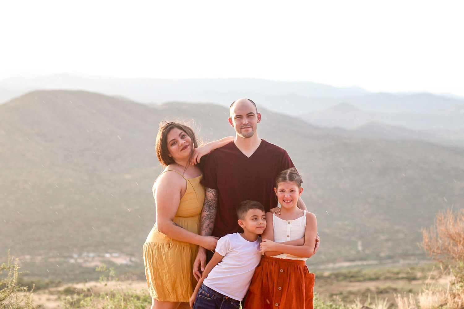 Happy family of four posing together with scenic mountain valley at sunset behind them.