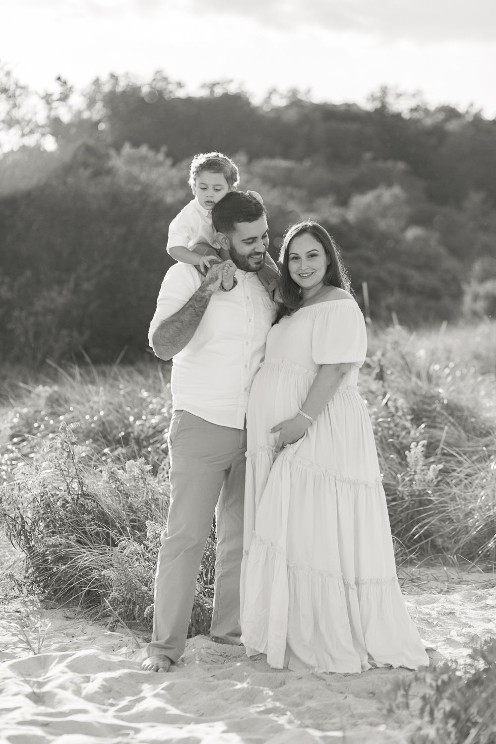 a black and white full body view of a family at the beach during a maternity session by Paula Ortiz NY Family Photograph