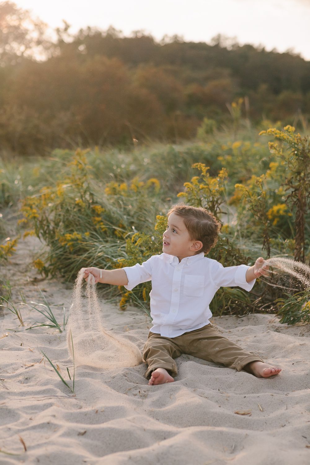 a toddler boy sitting and playing with sand during a golden hour session by Paula Ortiz NY Family Photography