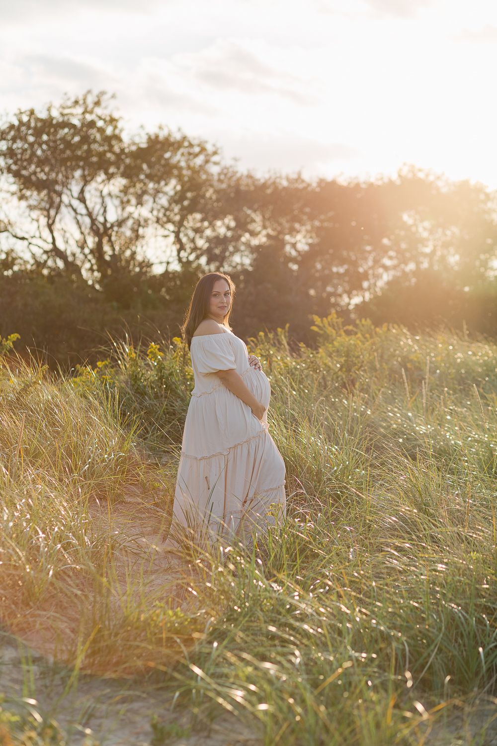 a light flare scene of a pregnant woman at the beach during a maternity session in Long island NY by Paula Ortiz