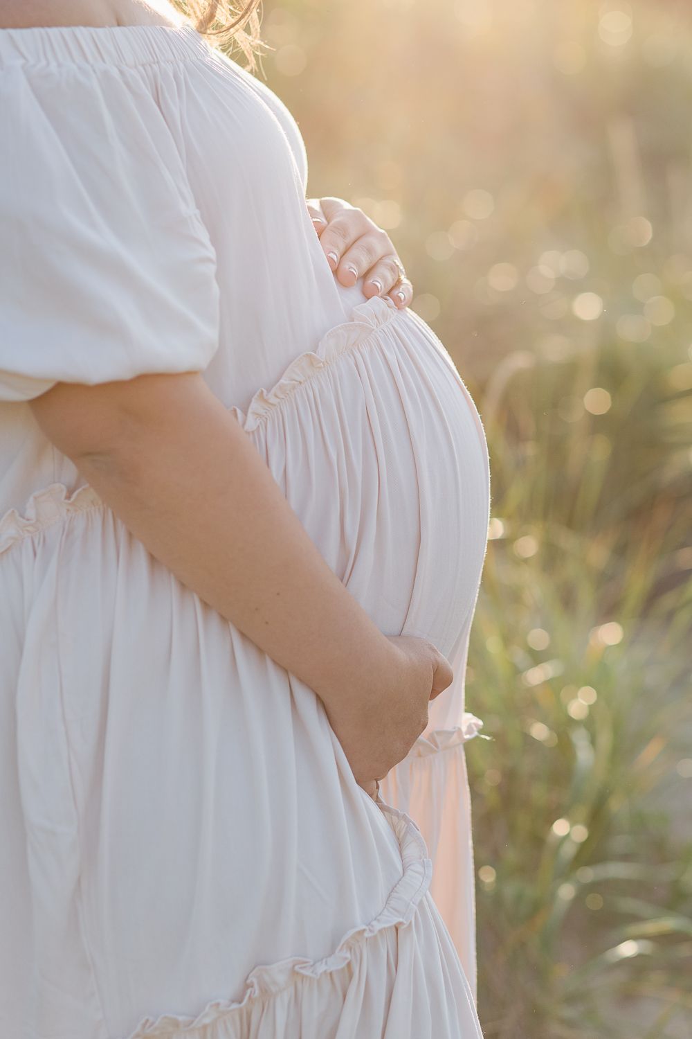 a close up view of a pregnant woman's belly bump with beautiful flare light photographed by Paula Ortiz NY Family Photos