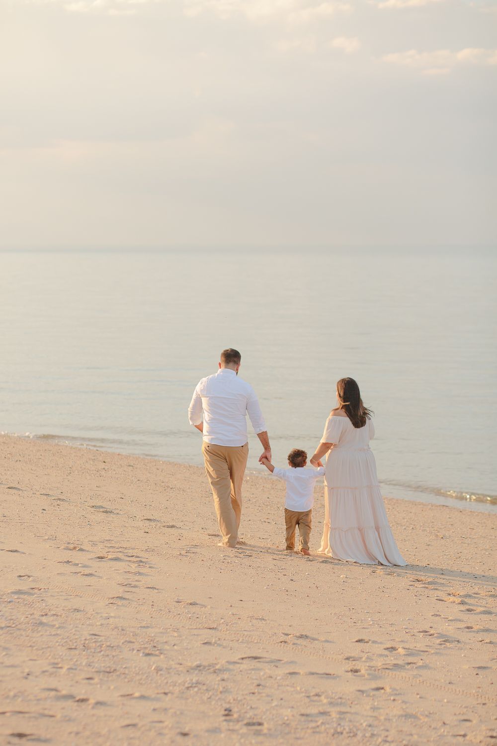 a family of three walks away along the shore line on a family beach session by NY Family Photographer Paula Ortiz