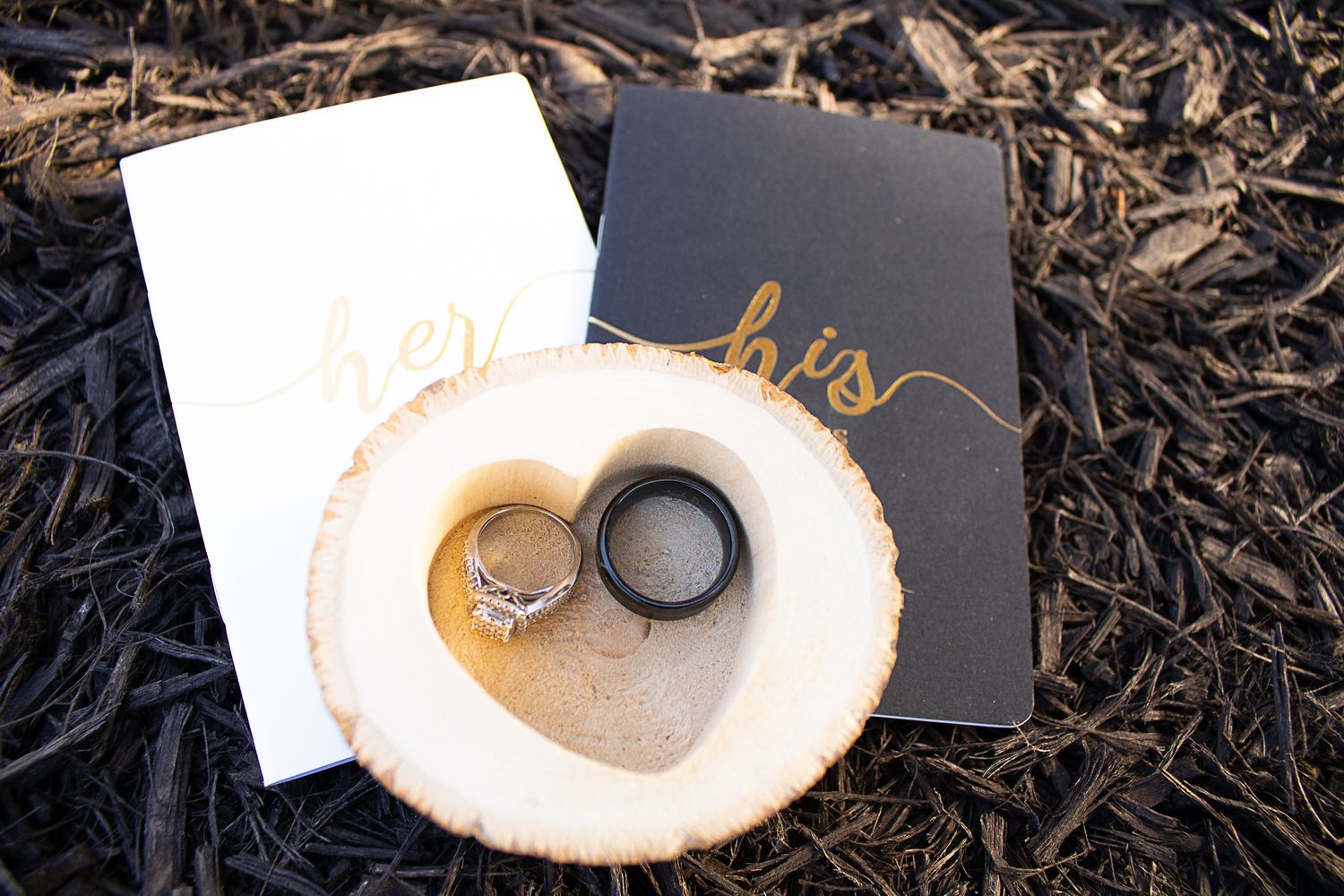 Wedding rings displayed on rustic wooden slice against dark background.