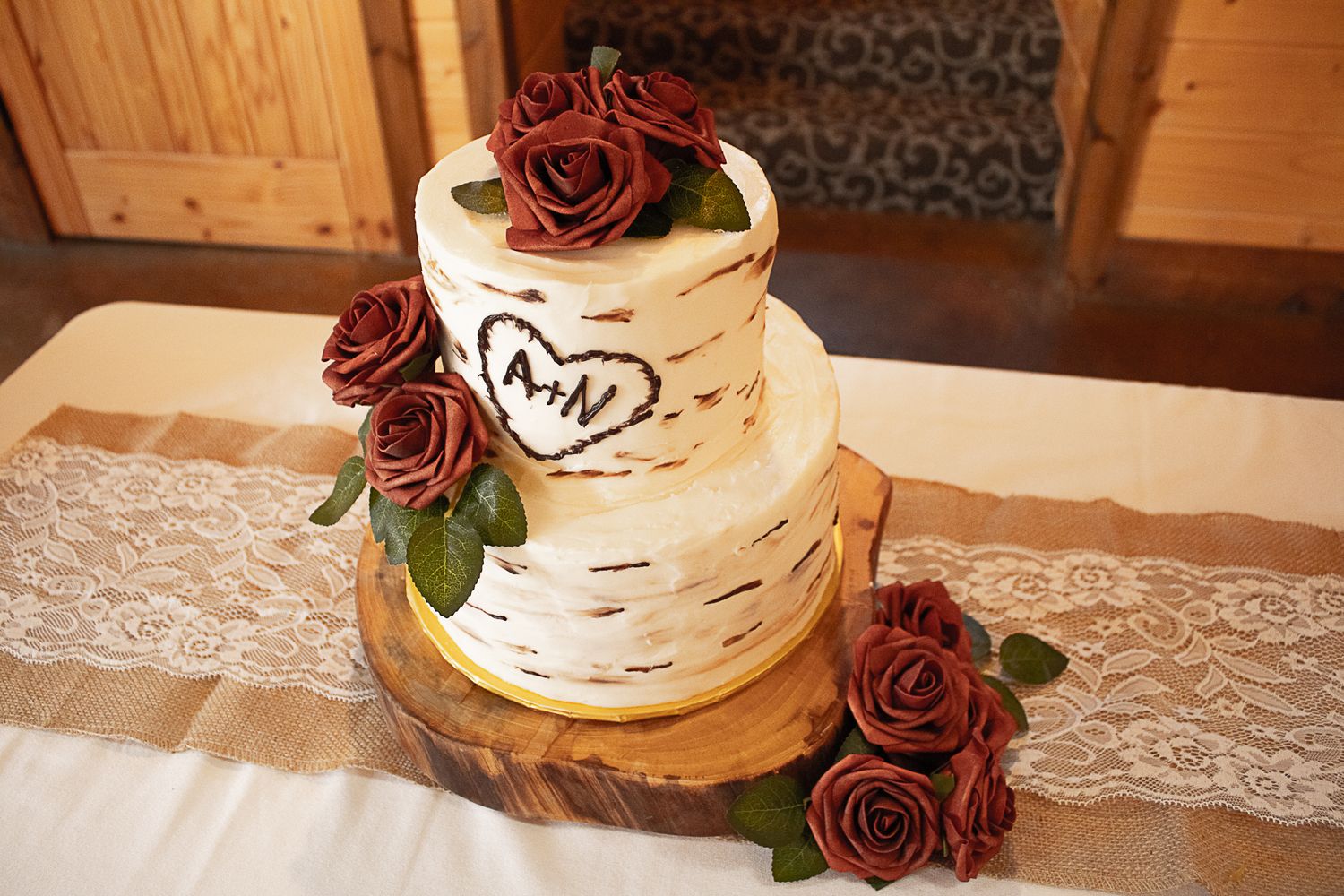 A rustic birch-themed wedding cake decorated with burgundy roses on a lace tablecloth.