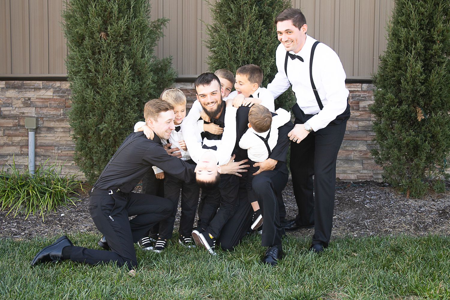 Groomsmen in black suits and suspenders huddled together outdoors.