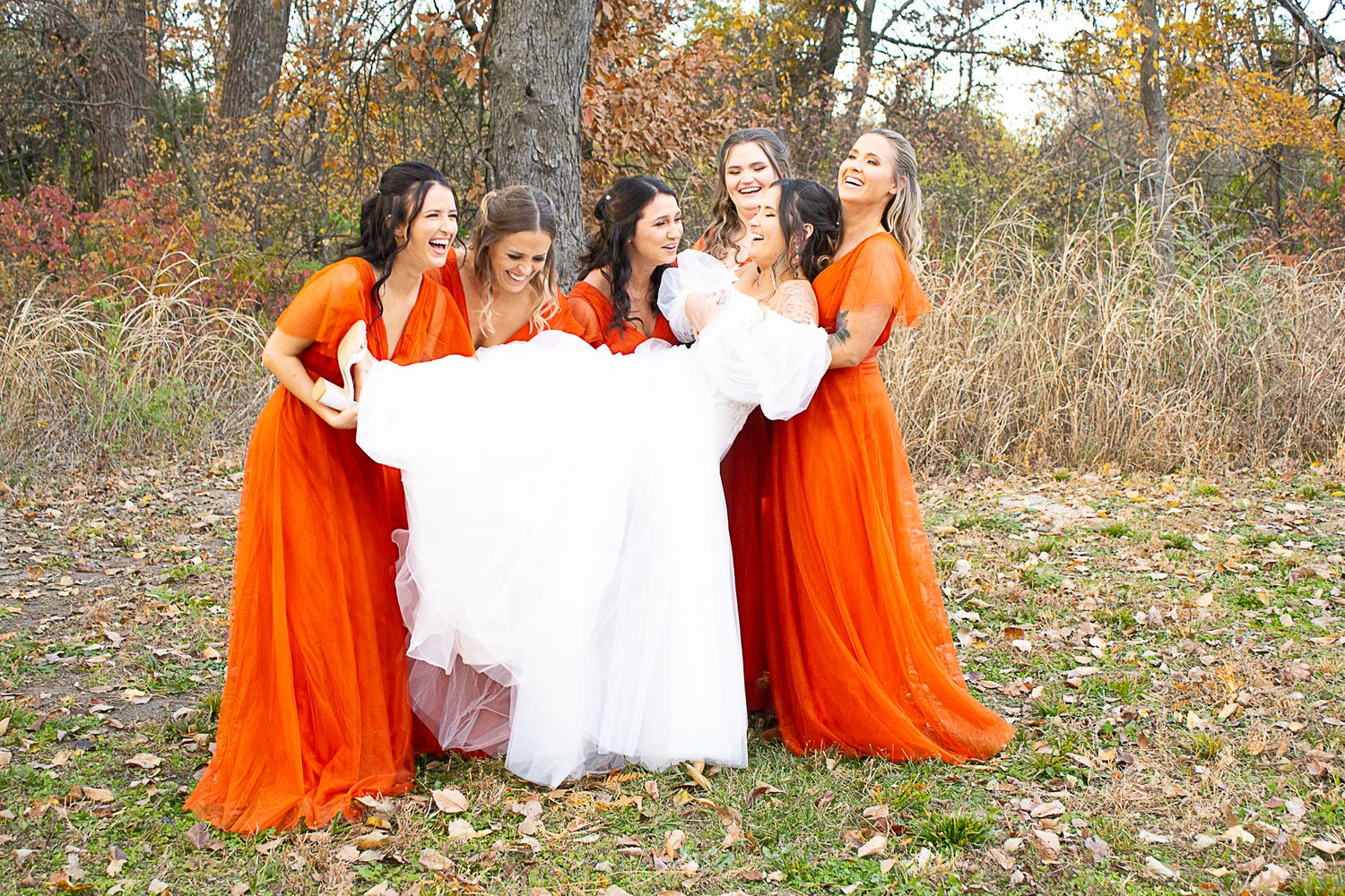 Wedding party posed in autumn setting with orange and white attire.