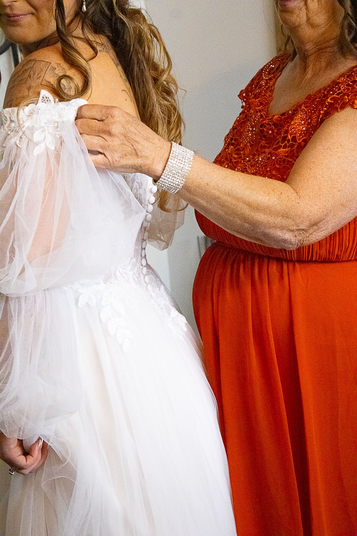 Close-up of a white wedding dress being adjusted, with someone in a red dress helping.