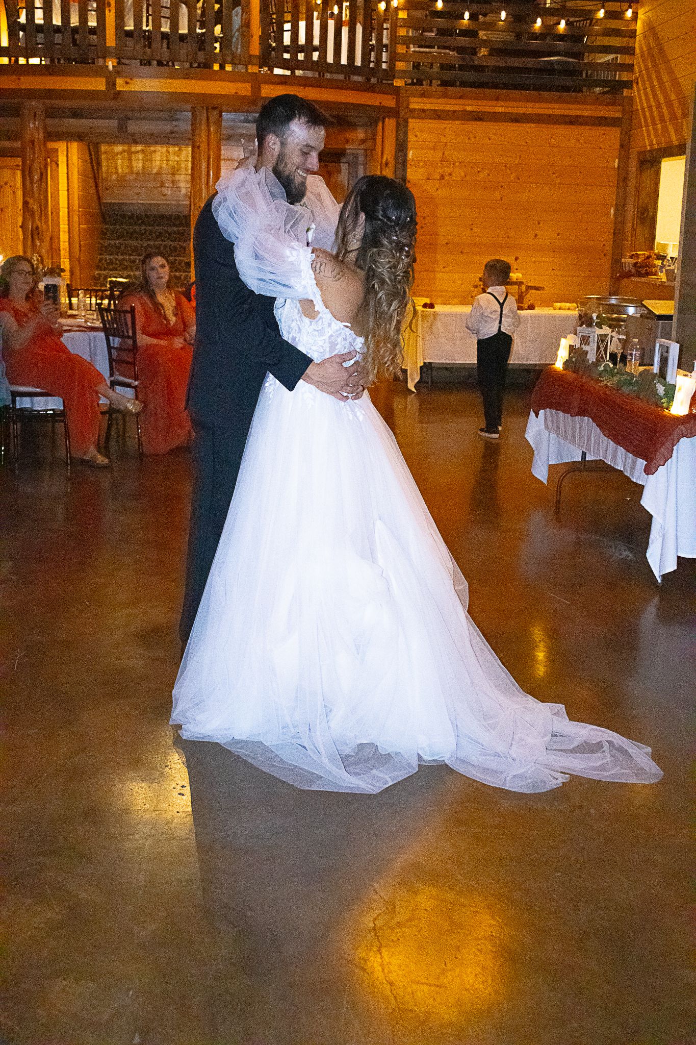 A couple sharing their first dance in a rustic wooden venue with warm lighting.