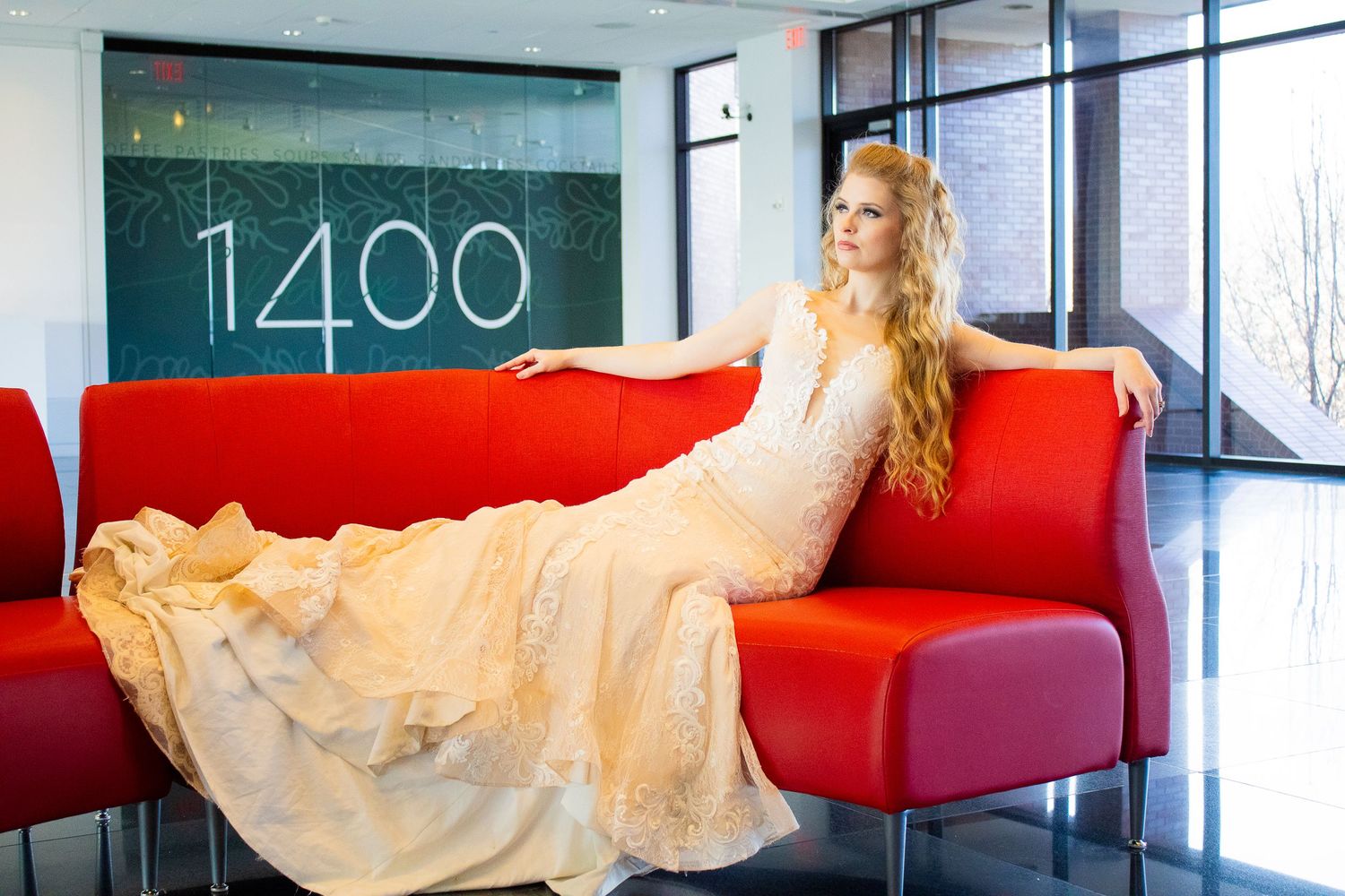 Woman in white dress lounging on a bright red modern couch in a contemporary office space.