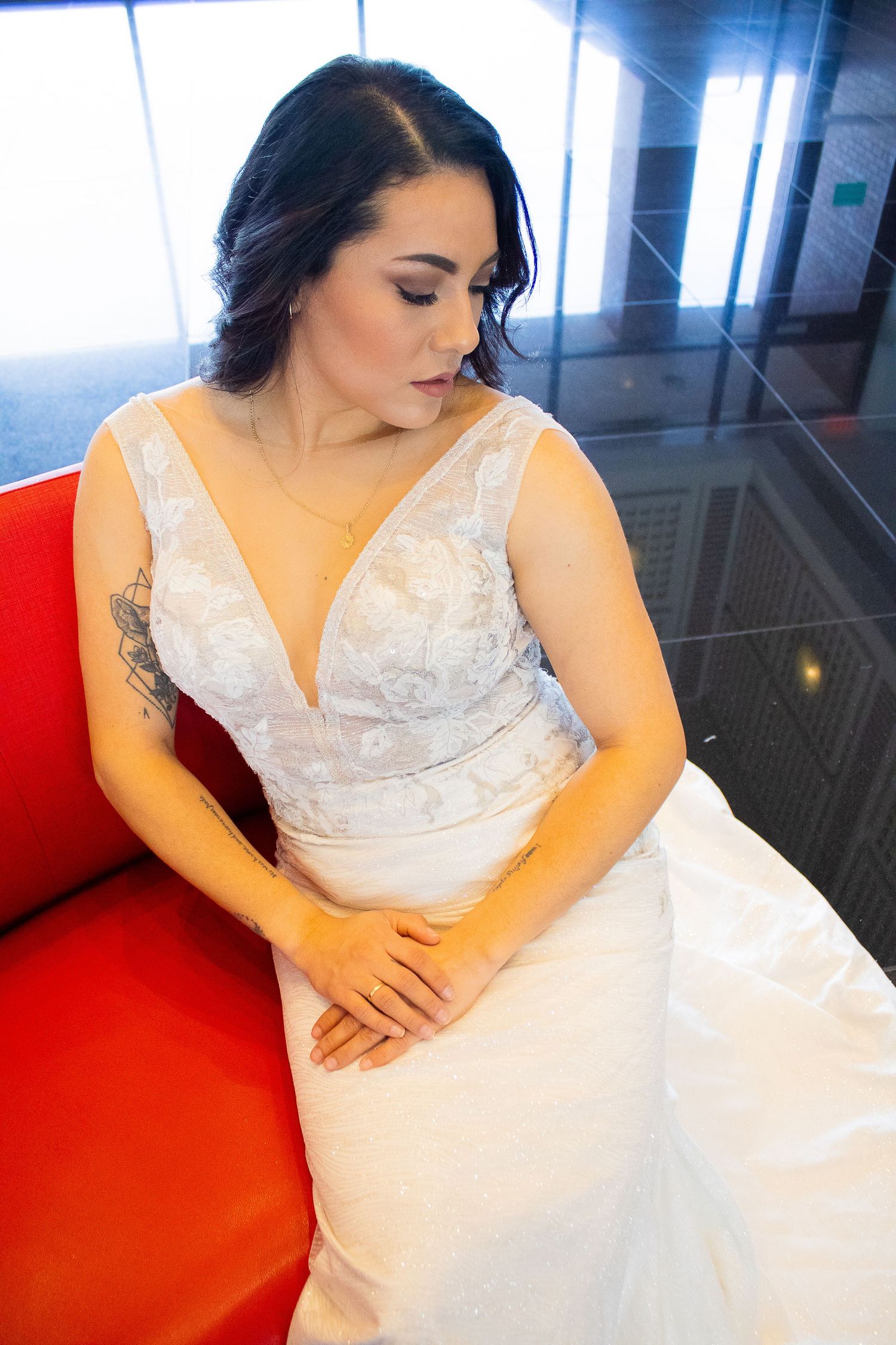 Bride wearing a white lace wedding dress reclining on a red couch.