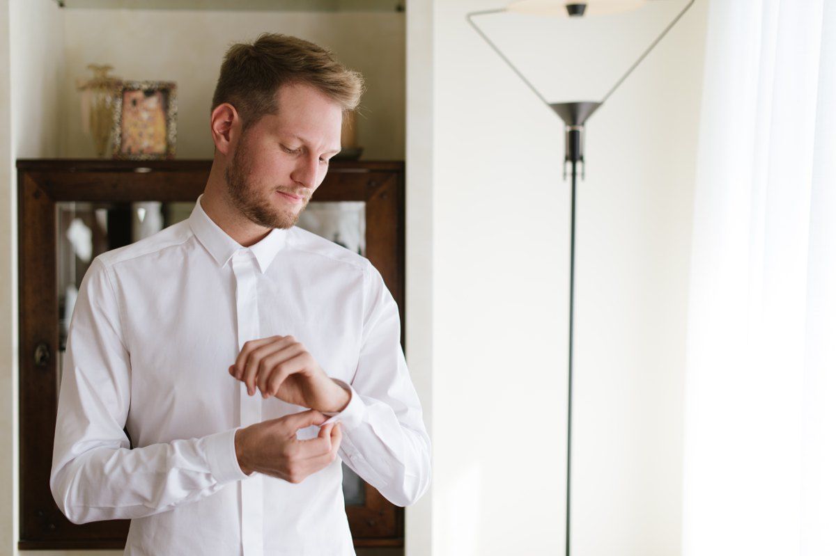 A person in a white dress shirt checks their watch while getting ready.