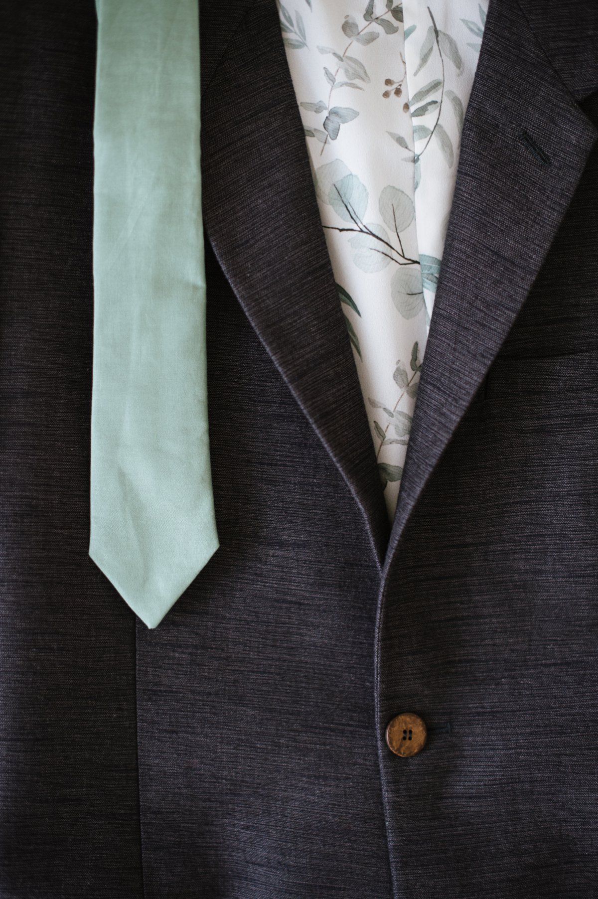 A close-up of a mint green tie and dark suit jacket with floral pattern lining.