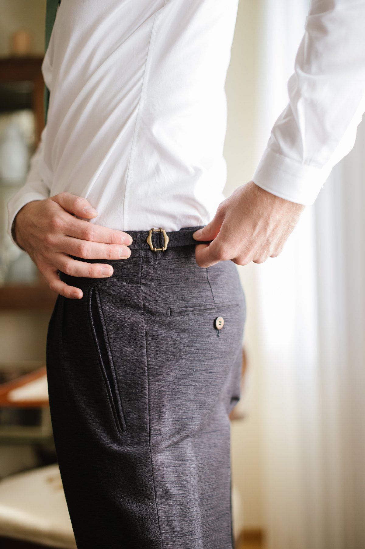 Close-up of hands adjusting a belt on dark grey dress pants.
