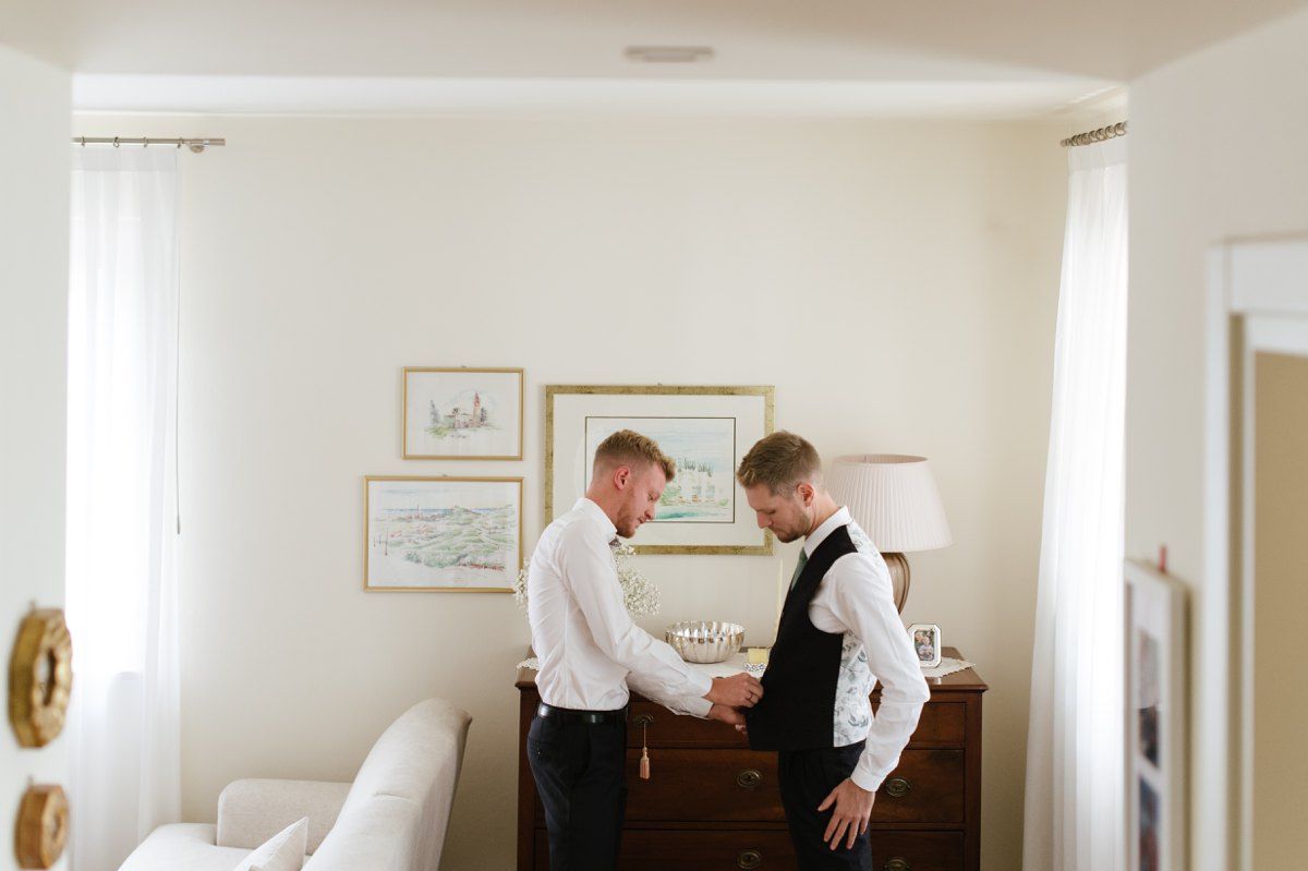 Two people in formal attire interact by a wooden dresser.