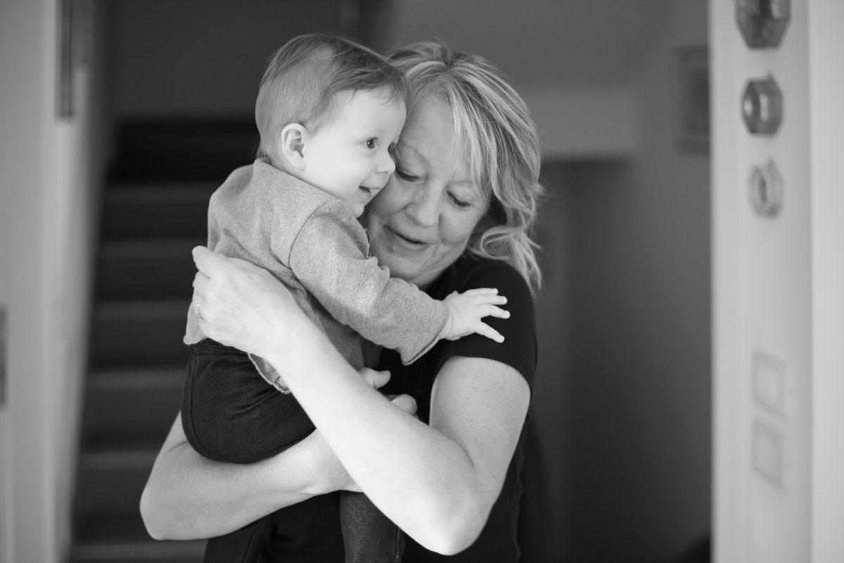 Black and white image showing tender moment between parent and baby embracing in intimate indoor setting.
