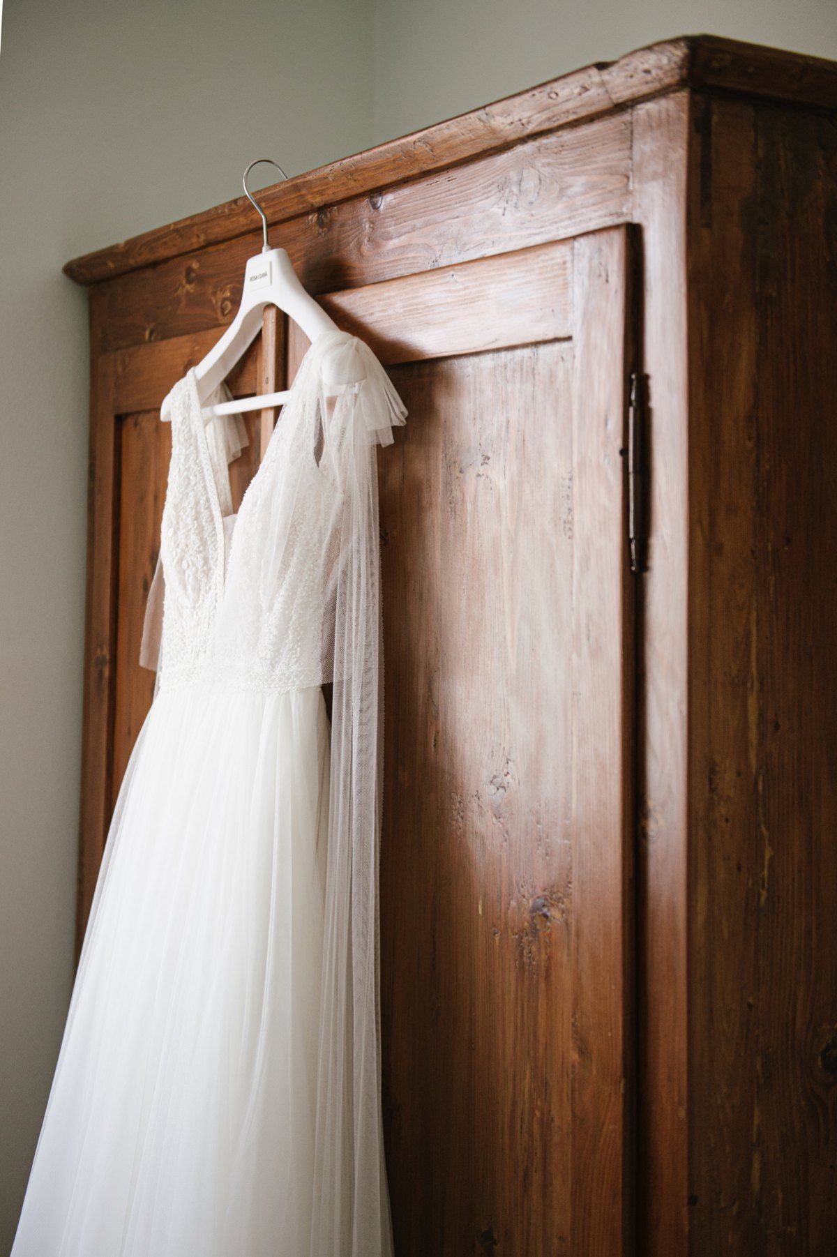 White wedding dress hanging on wooden wardrobe in natural light.