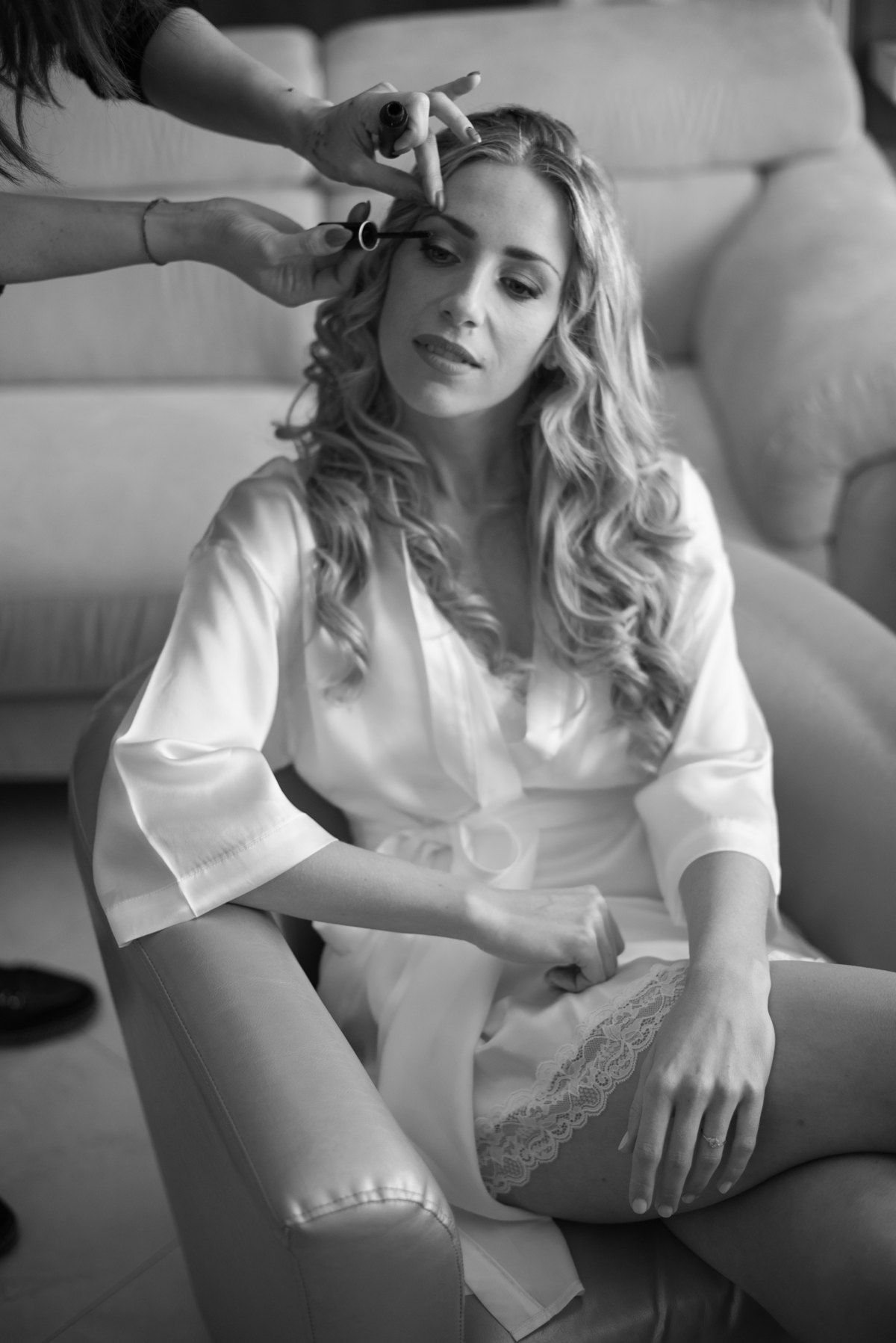 Black and white photo of person getting hair styled while sitting on couch in silk robe.