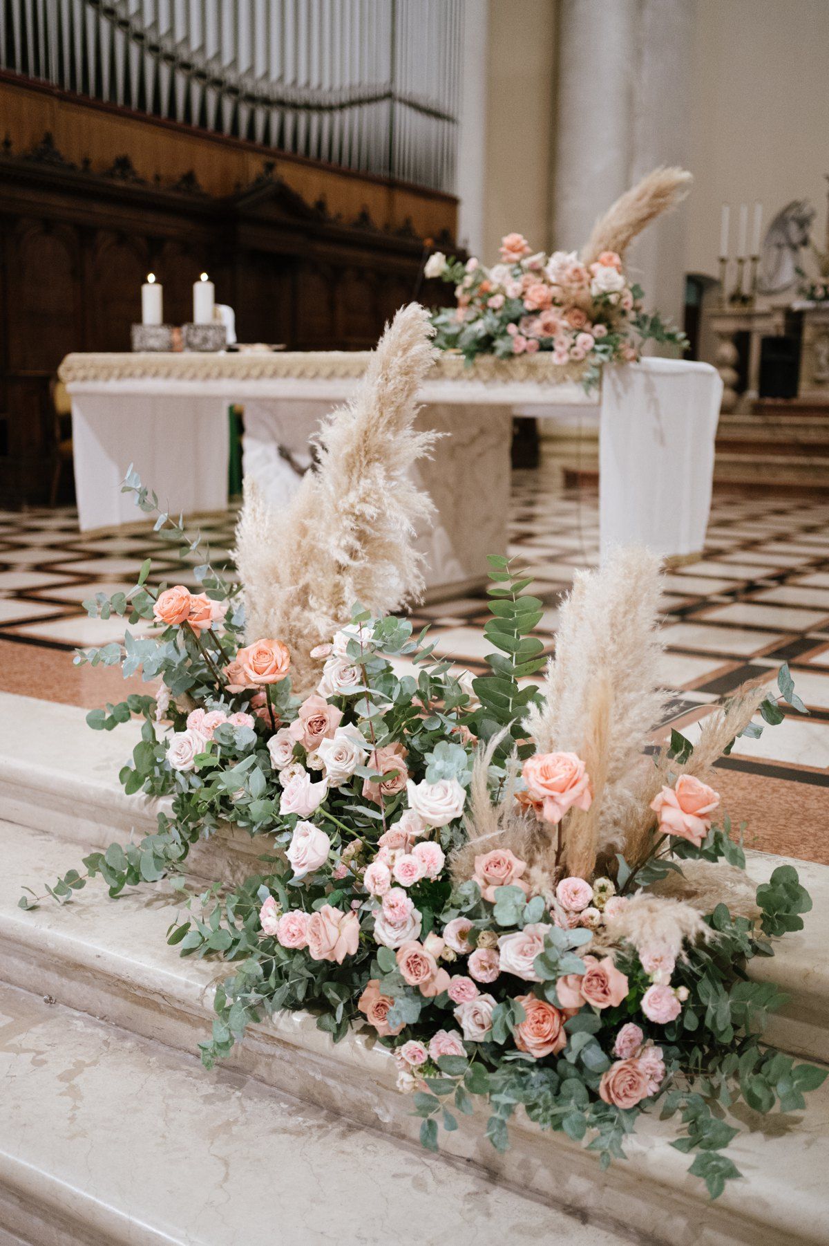 Romantic floral arrangement with pink roses and pampas grass decorating church steps.