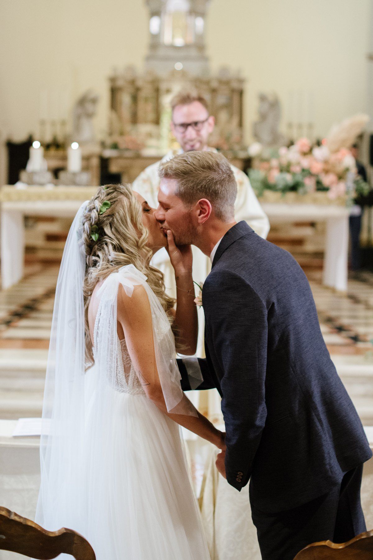 A tender wedding kiss shared at the altar of a beautifully decorated Italian church.