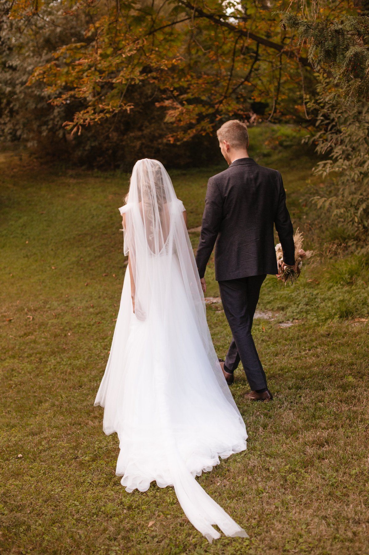 A romantic autumn wedding scene with a couple walking through fallen leaves.
