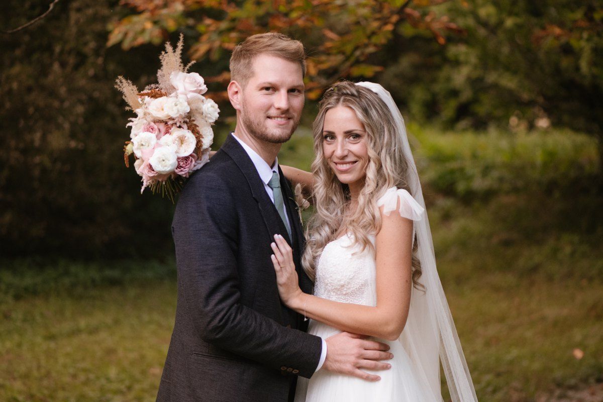 Wedding couple posing with pink bouquet in autumn garden setting.