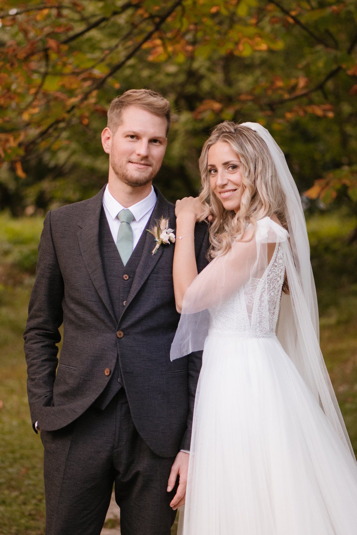 Stylish autumn wedding portrait with couple against fall foliage background.