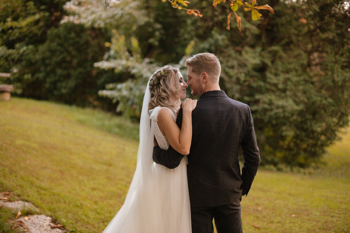 Bride and groom share a tender moment on their autumn wedding day against natural foliage.