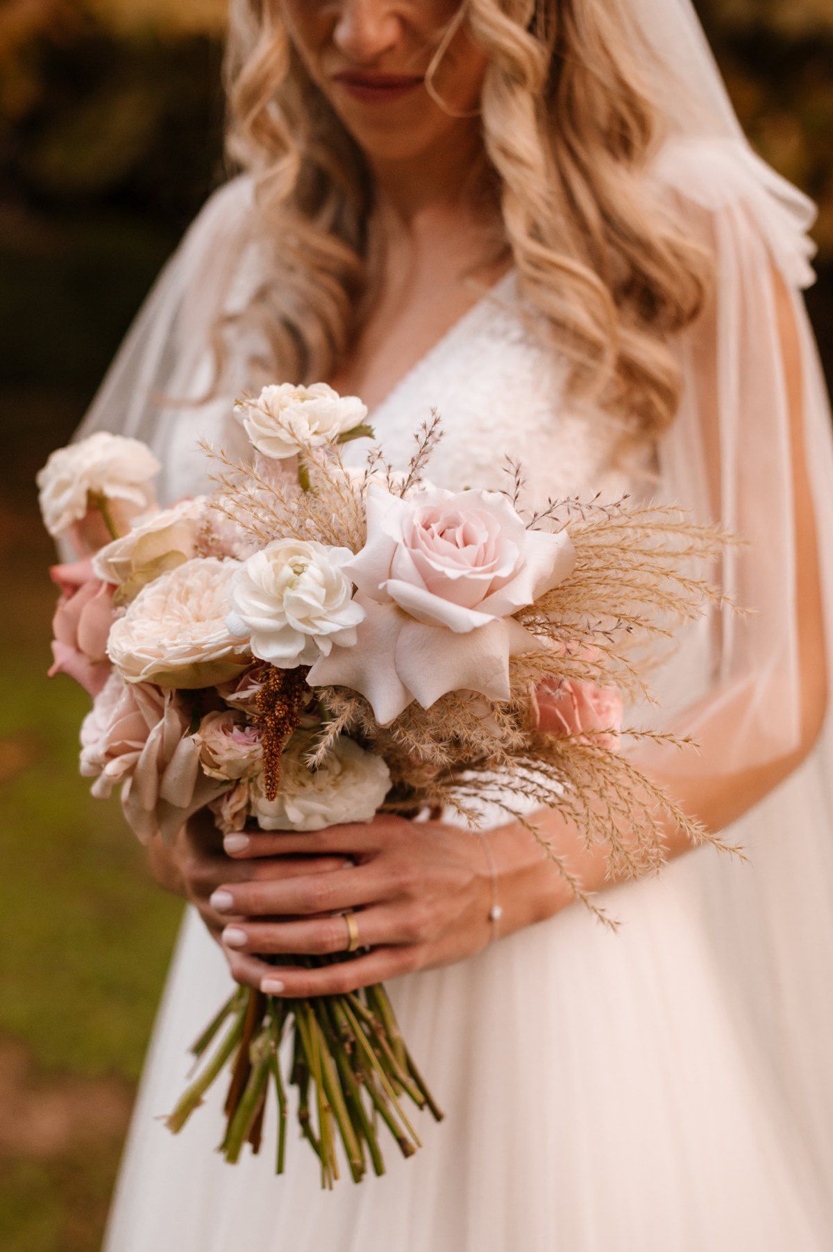Close-up of bridal bouquet with blush roses and dried flowers held by bride in white dress.