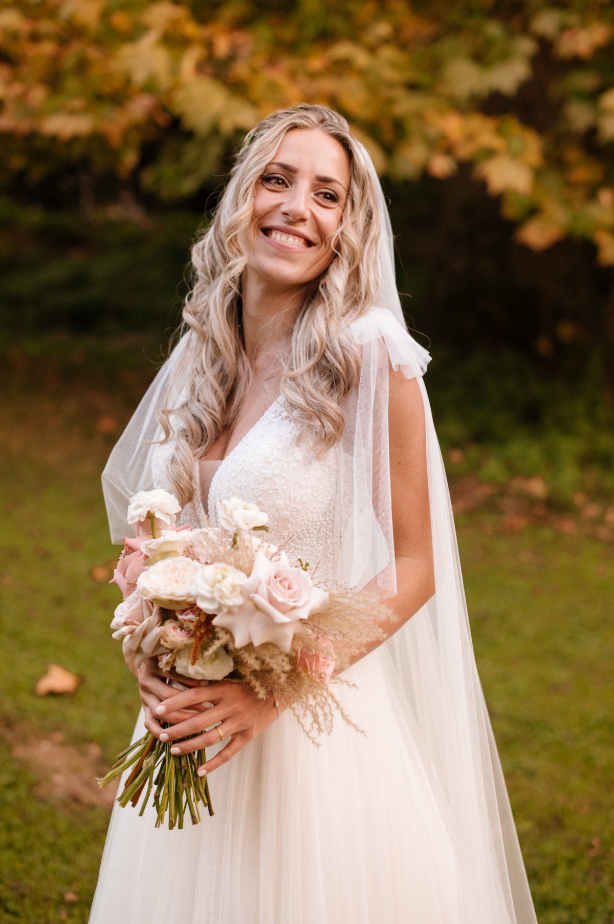 Wedding portrait of a bride in a white dress holding a pink bouquet during autumn.
