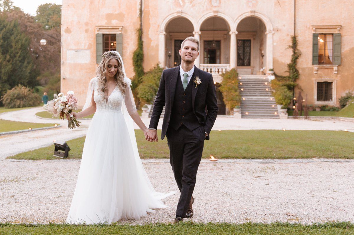 Newlyweds walking hand in hand outside a Mediterranean-style villa.