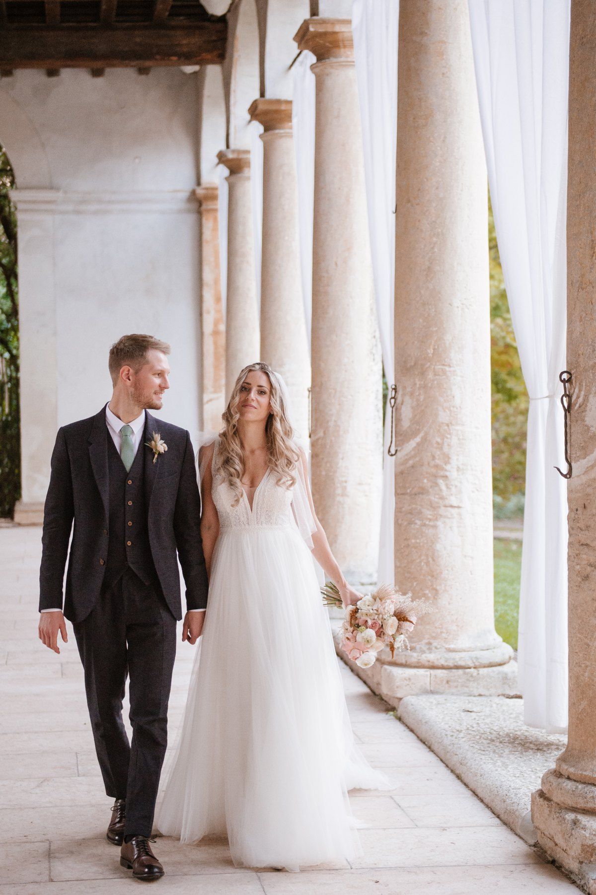 Elegant wedding couple walking along a columned portico.