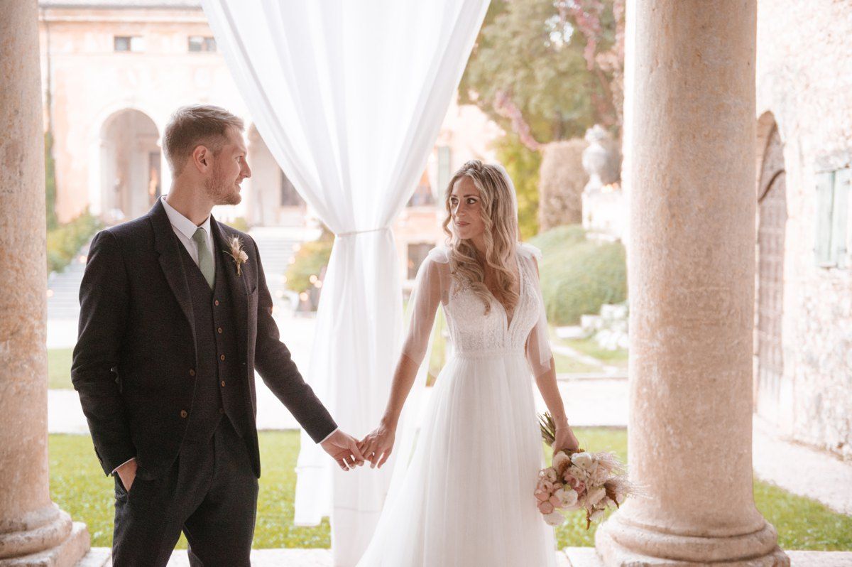 Candid wedding photo of couple holding hands under classical architecture.