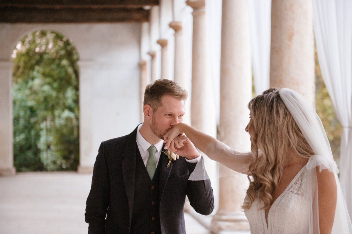 Sweet romantic gesture between newlyweds in a columned hallway.