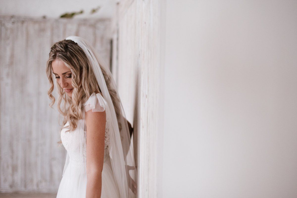 Side profile of bride in white gown against rustic white wall.
