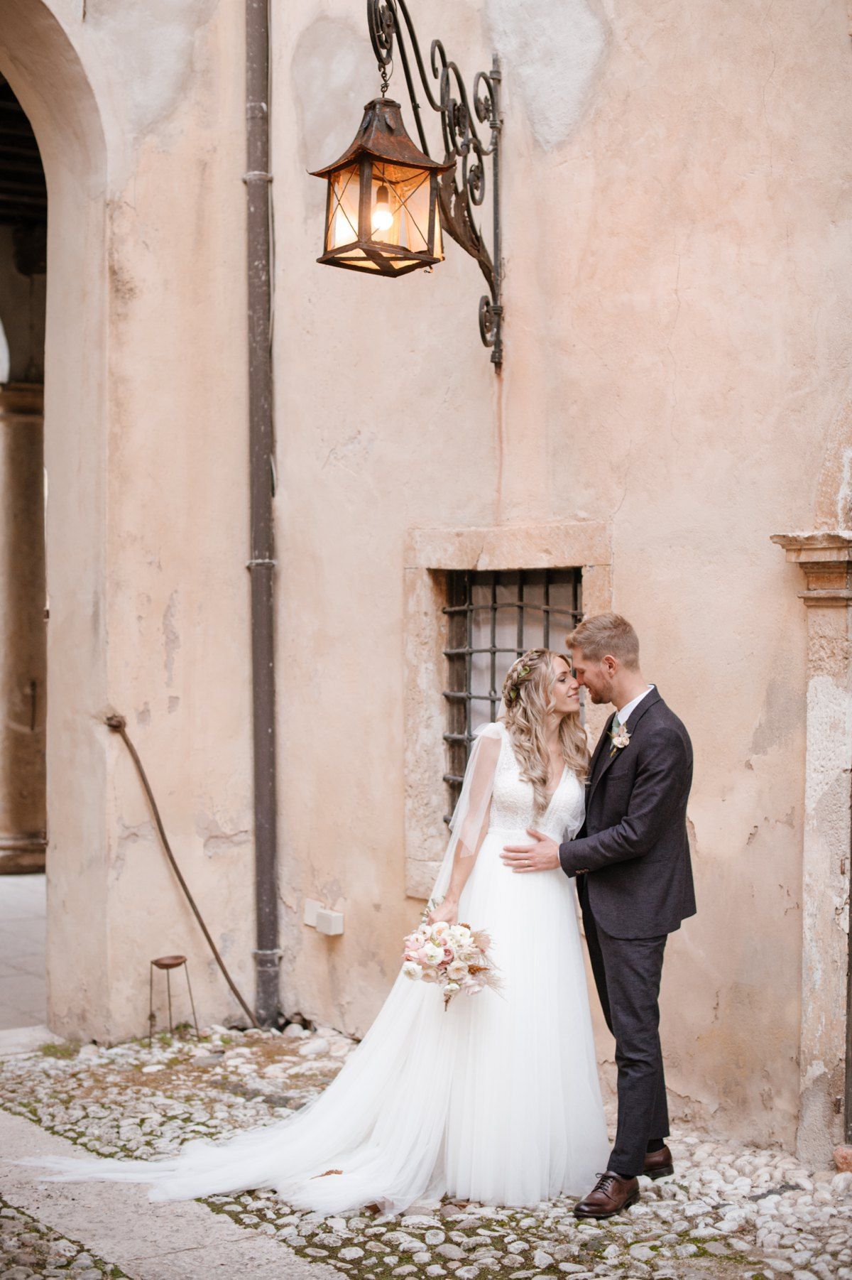 Romantic wedding portrait under vintage lantern against peach-colored wall.