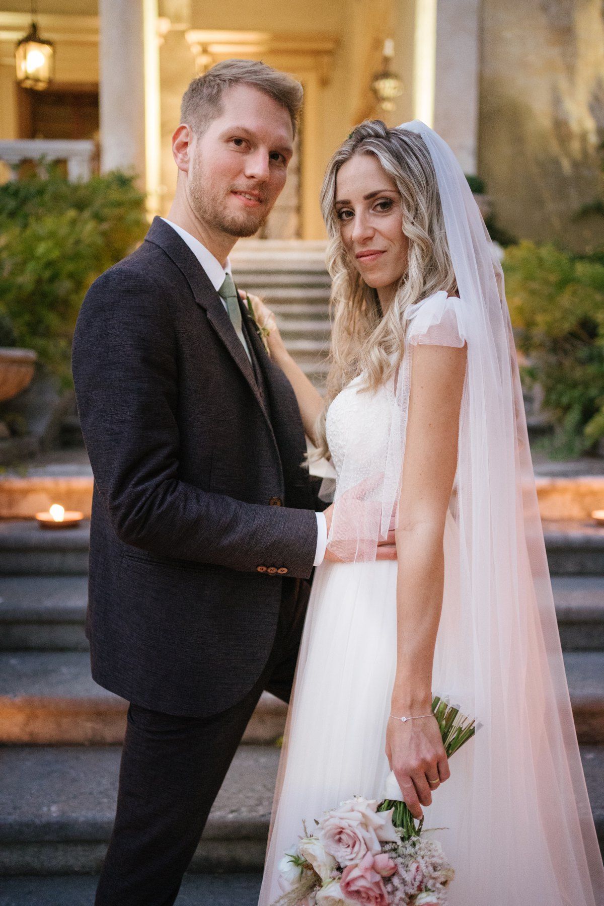 Elegant couple posing on historic villa steps decorated with glowing candles.