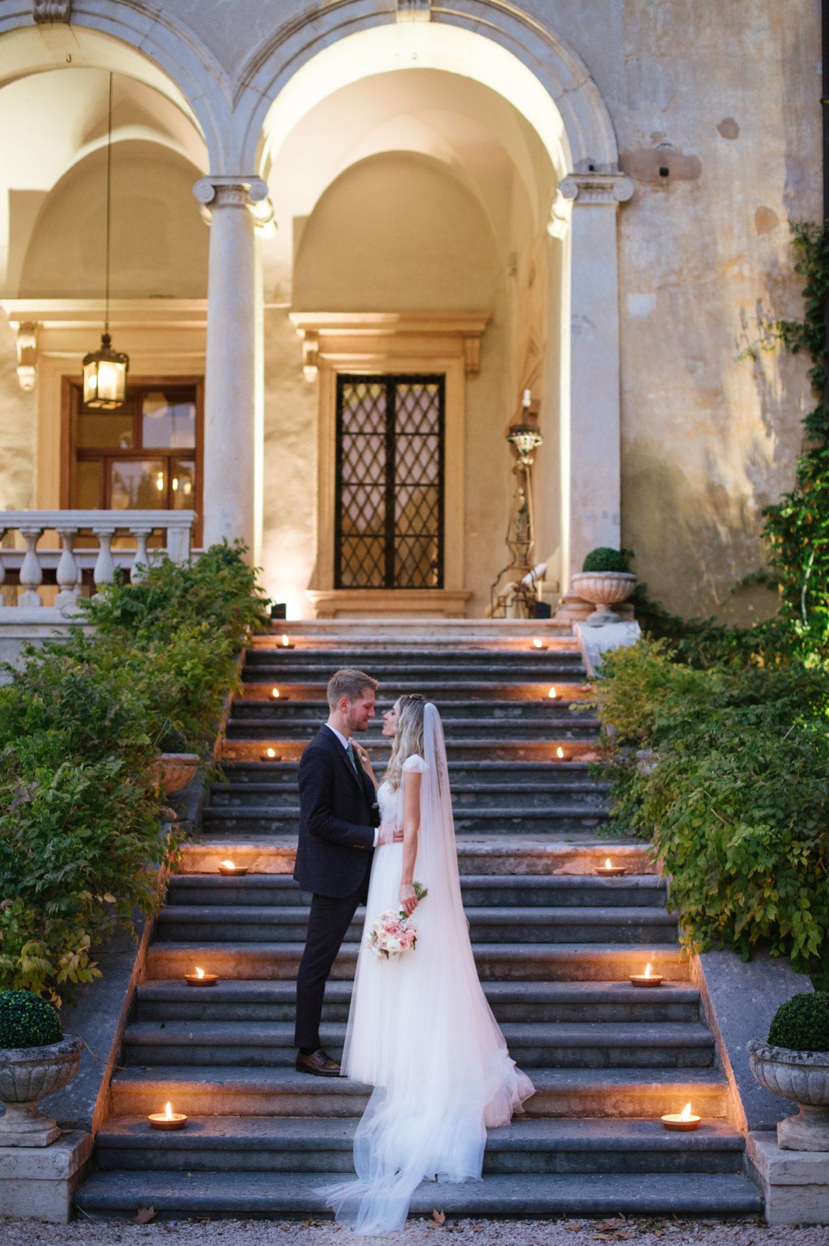Wedding couple standing on dramatic stone staircase illuminated by candlelight.