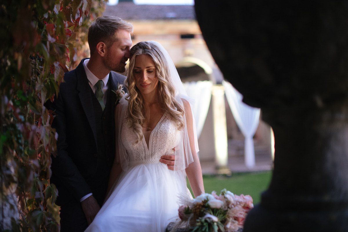 Intimate moment captured between newlyweds against ivy-covered villa wall.