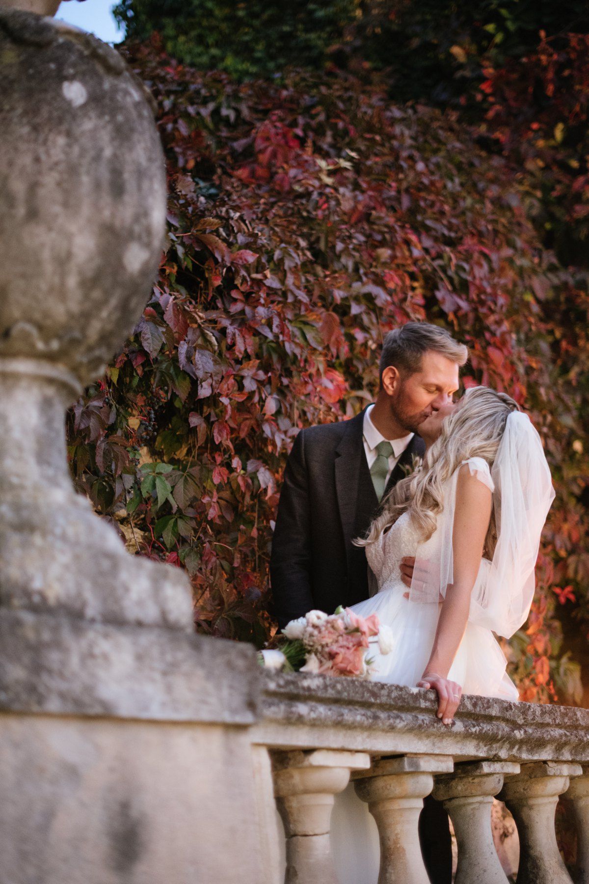 Romantic wedding moment on stone balcony with autumn ivy wall backdrop.