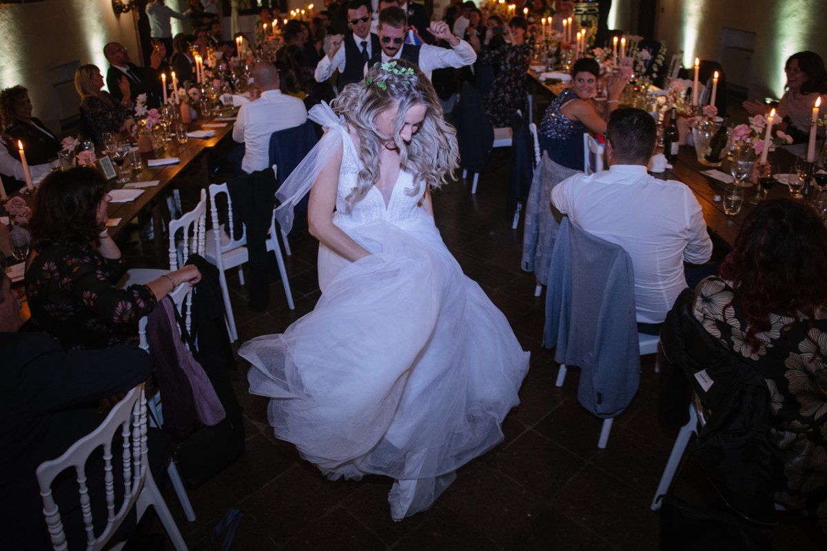 A wedding celebration with guests dancing in a candlelit reception hall.
