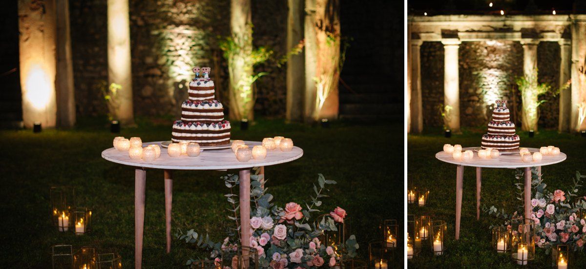 An elegant tiered wedding cake displayed against illuminated stone ruins with glowing candles.