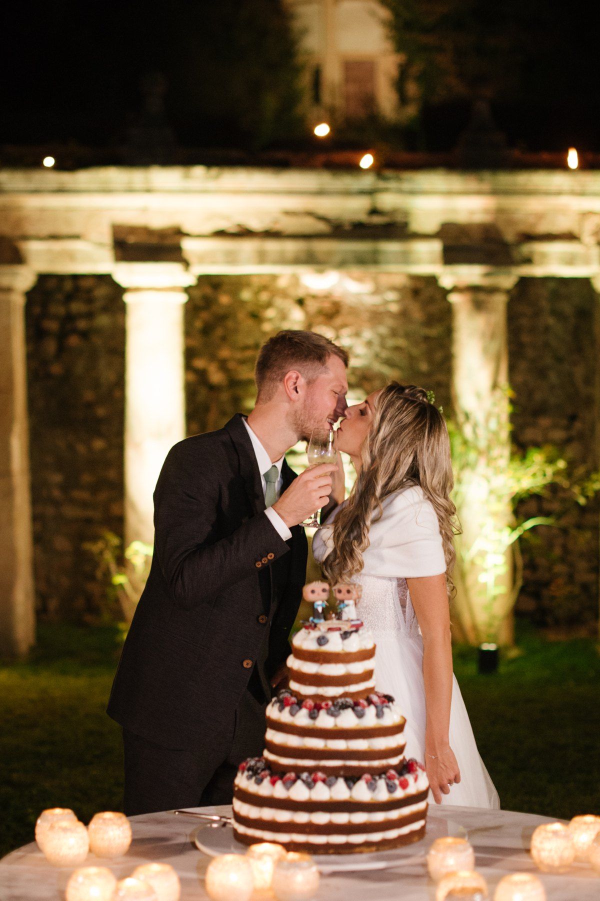 A romantic wedding cake cutting moment in front of illuminated stone columns.