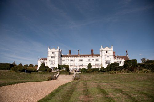 Expansive white mansion estate with Tudor-style architecture set against blue sky.